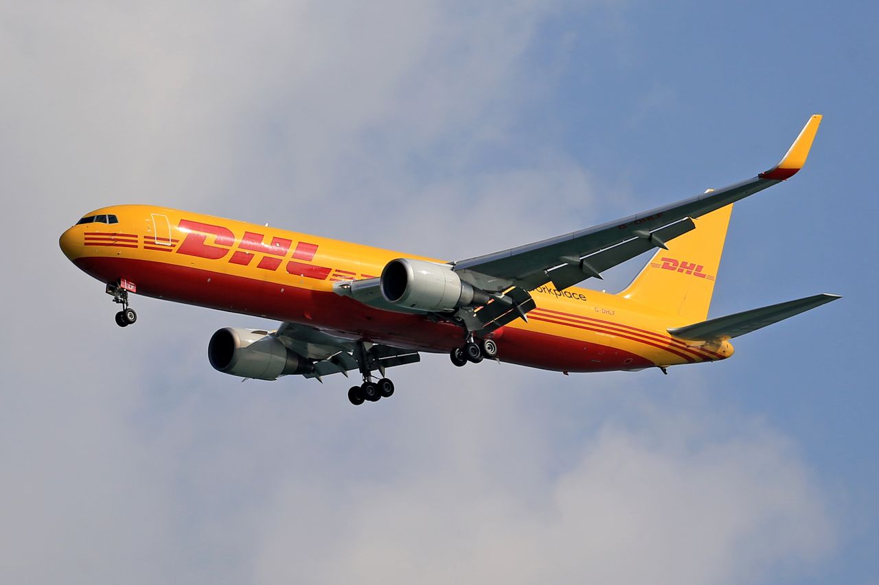 A DHL cargo airplane flying high against a clear blue sky, showcasing logistics and air transport.
