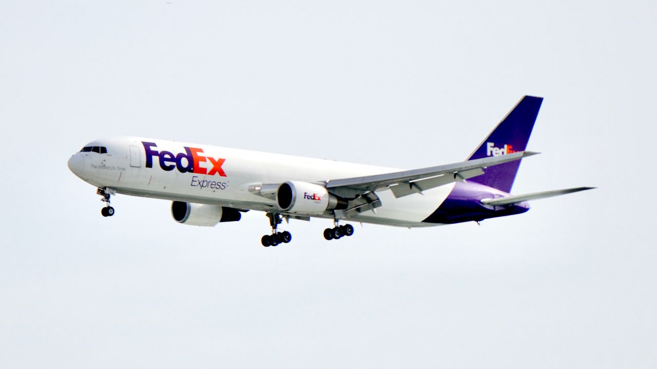 A FedEx cargo plane flying in daylight with a clear blue sky backdrop, showcasing logistics and air travel.